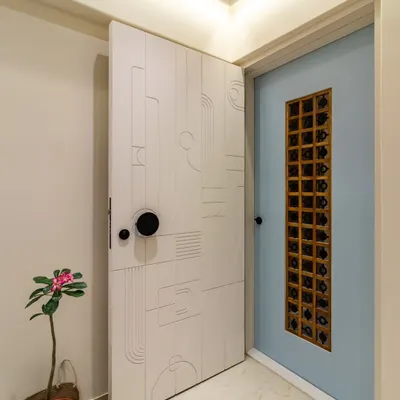 A modern and minimalist main door and safety door combination. The safety door features abstract routed lines, while the inner door has a unique artistic metal grill, creating a layered and intriguing entrance.