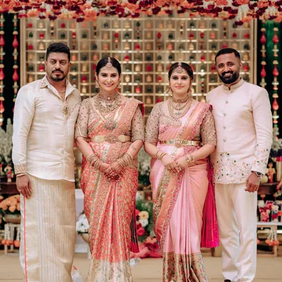 A beautiful family portrait from a naming ceremony. The sisters are coordinated in our bespoke pink and peach Kanchipuram silk sarees with heavily embroidered blouses, creating a harmonious and elegant look.