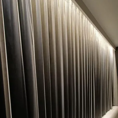 A close-up of a wall grazing technique applied to curtains. A concealed linear light fixture washes down the fabric, highlighting the deep folds and creating a beautiful, dramatic gradient from light to dark. This adds depth and a sense of luxury to the wall.