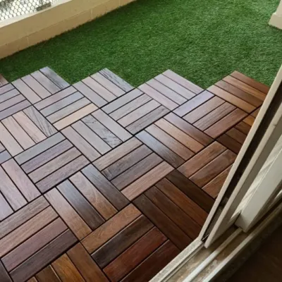 A finished balcony floor using a combination of interlocking wood tiles and artificial turf. The tiles are laid in a herringbone pattern to create a custom, high-end look.