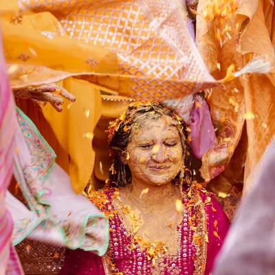 A blissful moment during the Haldi ceremony as the bride is covered in turmeric paste and flower petals under a traditional cloth. This image is full of color, texture, and pure happiness.
