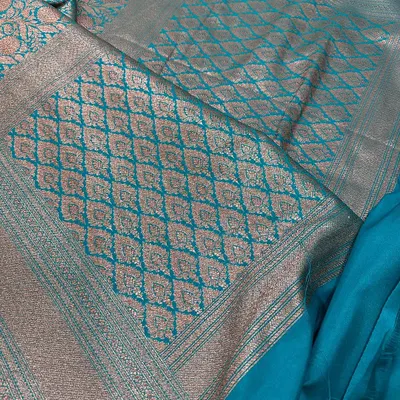 A complete look at this beautiful teal blue Banarasi silk saree. The rich pallu features a diamond-patterned jaal weaving in antique gold zari.