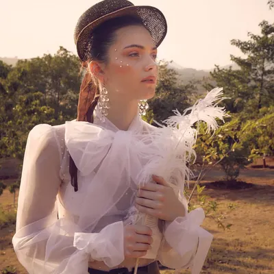A poetic portrait from the "White Rose" campaign for Starch Label. The styling features a sheer blouse with a large bow, a vintage-style hat, and a feather prop to create a dreamy and romantic character.