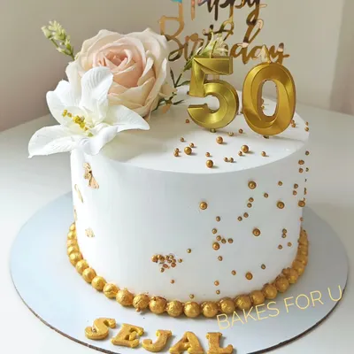 A beautiful cake for a 50th birthday, decorated with fresh flowers, gold sprinkles, and elegant gold numbers. The white and gold color scheme creates a classic and sophisticated look.