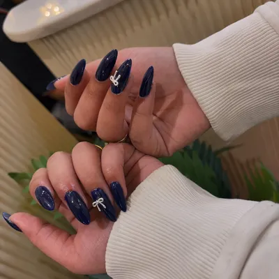 A simple yet chic design. We've elevated these glossy, deep blue almond-shaped nails by adding a delicate, white 3D bow accent.