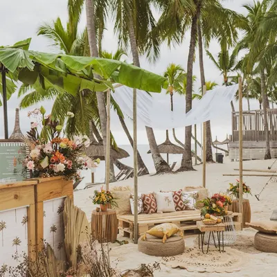 A relaxed beachside lounge in Mauritius, with a canopy made of banana leaves and seating made from wooden pallets and jute poufs.