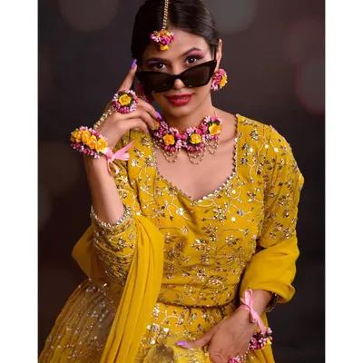 A modern and playful take on a traditional look. The model wears a stunning yellow lehenga and floral jewelry, but adds a pair of sunglasses for a touch of contemporary cool.
