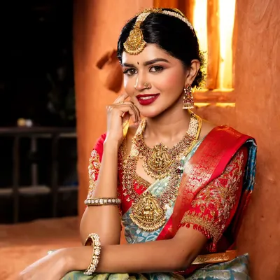 A classic South Indian bridal portrait. The makeup features a bold red lip, defined eyes, and glowing skin, perfectly complementing the traditional temple jewelry and silk saree.