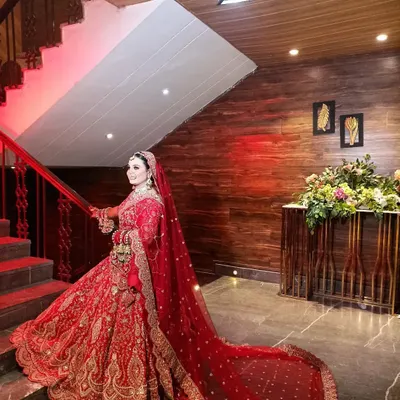 A stunning bridal portrait in a royal red lehenga with a long trail, captured on a staircase to emphasize its grandeur.