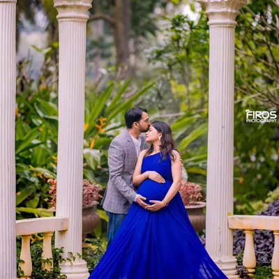 A tender moment between parents-to-be, framed by classic white pillars in a garden setting. The royal blue gown adds a pop of color, highlighting the beautiful baby bump in this serene maternity photograph.