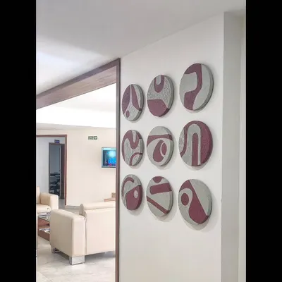 This custom art installation features a set of nine circular, textured panels. The abstract maroon patterns on the grey, textured base create a striking 3D effect on the wall of this modern living space.