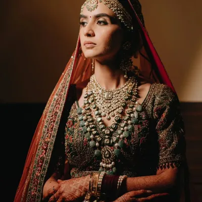 A breathtaking close-up of the bride in her royal attire, her gaze thoughtful and serene. The warm lighting highlights the intricate details of her jewelry and outfit.