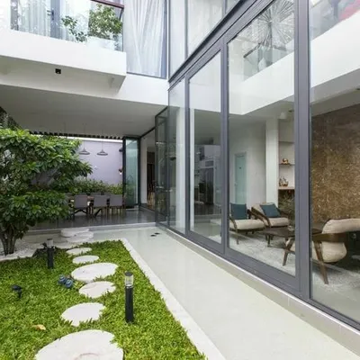 This is a semi-indoor garden that connects the home's interior with the outdoors. During the day, it's a bright, sunlit space with a natural lawn and stone pathway, viewed through large glass walls.
