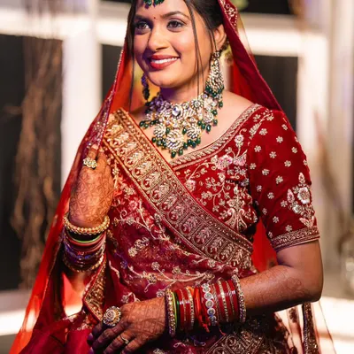 A radiant North Indian bride in a traditional red velvet lehenga. The airbrush makeup provides a flawless base that complements the heavy embroidery and jewelry.