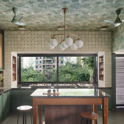 This kitchen is a celebration of pattern and texture. The botanical wallpaper on the ceiling and the hand-painted tiles create a rich, layered effect, while the deep green cabinetry and large island ground the space, making it feel both grand and inviting.