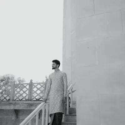 A stylish black and white portrait of the groom in his traditional attire. The architectural background and his confident pose create a modern yet timeless look.