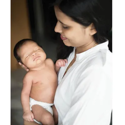 Capturing the sleepy, content face of a newborn is what in-home lifestyle sessions are all about. This image focuses on the baby's peaceful expression while being held securely in his mother's arms, a memory to cherish forever.