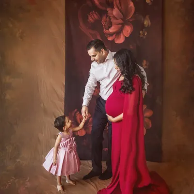 A beautiful family portrait awaiting their new arrival. The mother's flowing red gown is stunning against the artistic backdrop, and the connection with her daughter and husband is palpable.