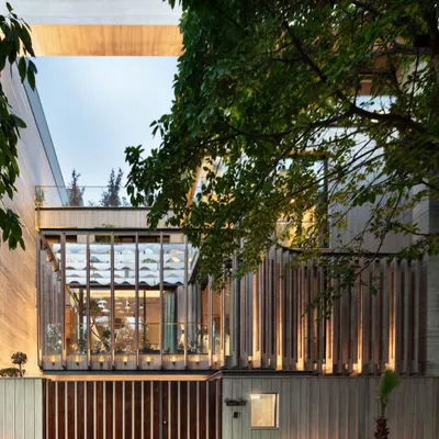 The facade of our Punjabi Bagh residence, seen here at dusk, highlights the dialogue between solid and void. The illuminated glass box, shielded by a wooden screen, establishes a strong connection between the interior and the mature trees outside.
