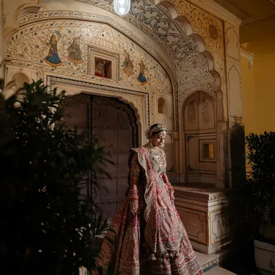 A stunning portrait of the bride, Aashi, standing in a beautifully lit archway at Mundota Palace, capturing the grandeur and solitude before the ceremony begins.