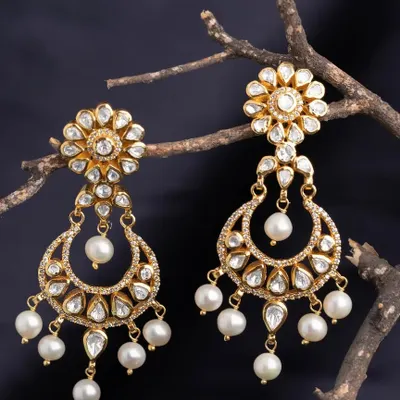 These stunning chandbali earrings are crafted with a floral stud and a crescent moon drop, both adorned with kundan-style stones and pearls. They are the epitome of royal elegance.