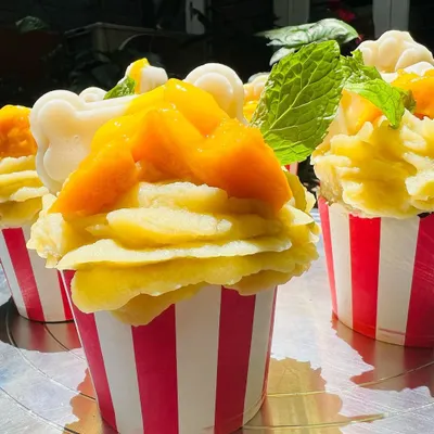 A batch of my seasonal Mango Tango pupcakes. They are topped with fresh mango chunks, a mint leaf, and a white jelly bone made from coconut.