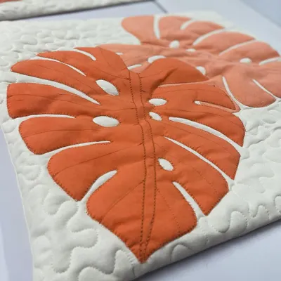 A close-up of a quilted cushion cover featuring a modern monstera leaf appliqué design with detailed stitching.