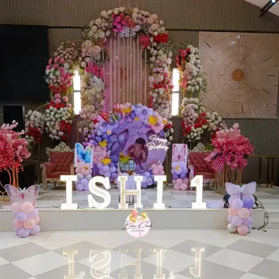 A grand stage decoration for a first birthday, featuring a massive floral arch and a butterfly-themed balloon setup with marquee letters.