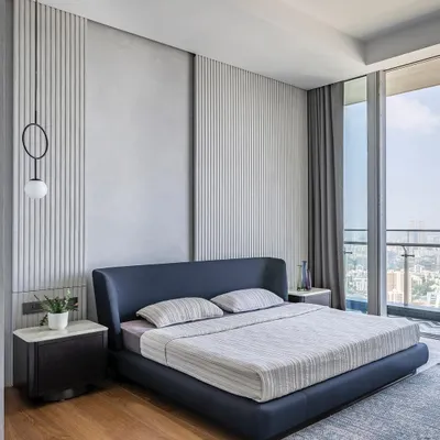 This minimalist master bedroom in 'The Grey House' overlooks the city and is designed for serenity. The feature wall combines smooth concrete texture with vertical fluting, creating a subtle play of light and shadow.
