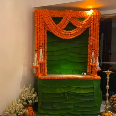 This is a classic South Indian inspired decor, featuring a structure made entirely of fresh banana leaves and draped with bright orange marigold garlands. It's a simple, elegant, and purely traditional way to set up your mandap.
