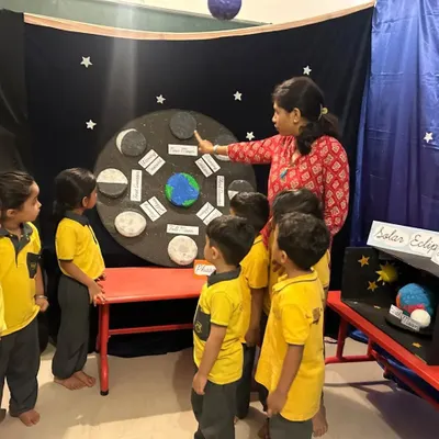 A teacher explains the phases of the moon to a group of curious students using a handmade model. We make astronomy accessible and fascinating, encouraging children to look up and wonder about the universe.