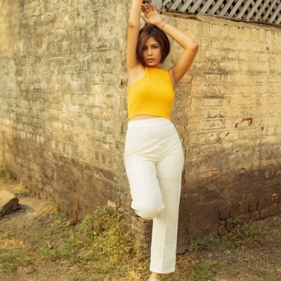 A fashion portrait taken during the golden hour against a rustic brick wall. The warm light on the model's yellow top creates a vibrant, eye-catching image.