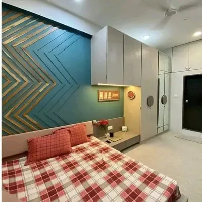 A bedroom interior featuring a unique chevron-patterned wooden headboard against a teal accent wall. The wardrobe and loft storage are seamlessly integrated for a clean finish.
