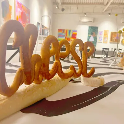 Where art meets appetite. For this unique event in an art gallery, we crafted a playful centerpiece with the word "Cheese" sculpted from bread, setting the stage for an interactive and memorable dining experience.