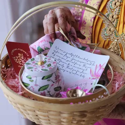 A return gift basket for a 'Valakappu' (baby shower) ceremony. It includes a floral tin, a handwritten thank you note, and other small tokens of appreciation for guests.