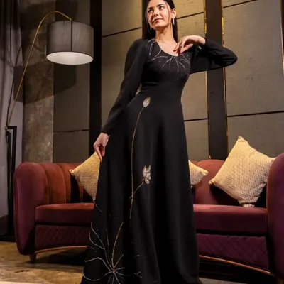 A full-length shot of a model in a black gown with delicate gold embroidery. The studio lighting is carefully placed to make the embroidery shimmer, highlighting the garment's premium quality.