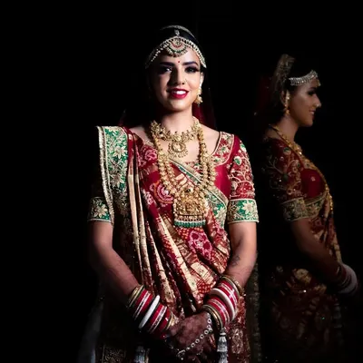 A stunning bridal portrait against a black background, with a reflection adding depth. The lighting perfectly highlights the intricate details of her traditional attire and jewelry.