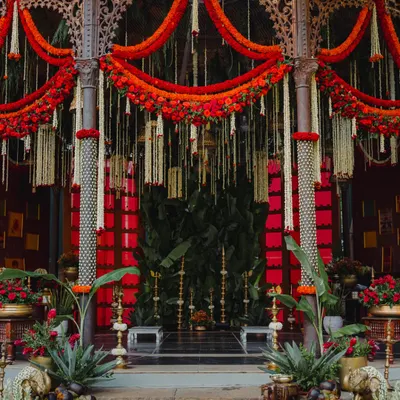 This mandap design is a tribute to South Indian royalty. The bold red backdrop, framed by traditional pillars and adorned with marigold and tuberose garlands, creates a space that is both grand and deeply rooted in heritage for the main wedding ceremony.