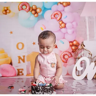A little boy enjoys his first birthday cake during a cakesmash session. The setup includes pastel balloons and "ONE" signs, creating a perfect scene for a milestone celebration.