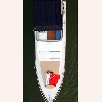 An epic aerial drone shot of Gurneet and Gurbani on a yacht in Goa. The bride's flowing red dress against the green sea creates a stunning, cinematic visual.