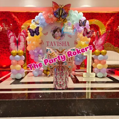 Here is the full view of a beautiful butterfly-themed first birthday I did. The setup includes a circular backdrop with the baby's name, a pastel balloon arch, large butterfly foils, and a light-up marquee number.