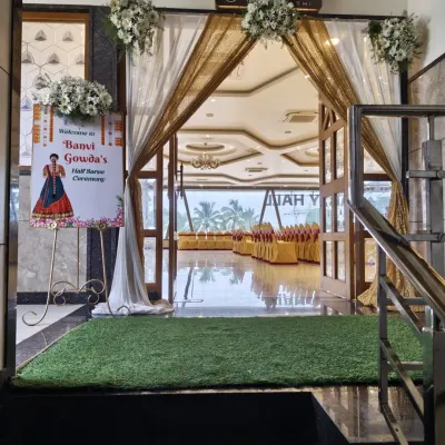 A lovely entrance for a Half-Saree ceremony. The doorway is draped with elegant white and gold fabric, and a personalized welcome sign with a custom illustration greets the guests.