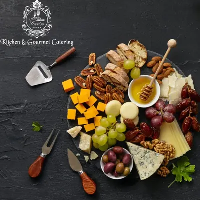 A classic charcuterie and cheese board, beautifully styled on a dark slate platter. It features a mix of hard and soft cheeses, nuts, dates, and honey, perfect for any gathering.