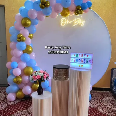 An "Oh Baby" decoration for a baby shower, with a pink, blue, and gold balloon arch against a white circular backdrop.