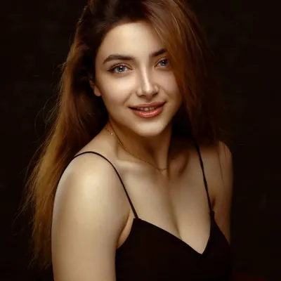 A classic beauty portrait with a warm, inviting smile. The soft lighting and simple black top put all the focus on her natural elegance and bright expression.