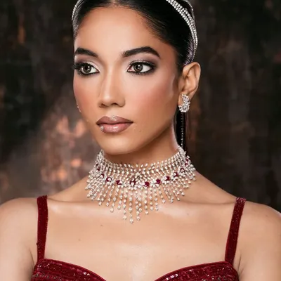 A classic beauty portrait. The focus is on the luminous skin, sharp winged eyeliner, and the sparkle of the ruby and diamond choker.