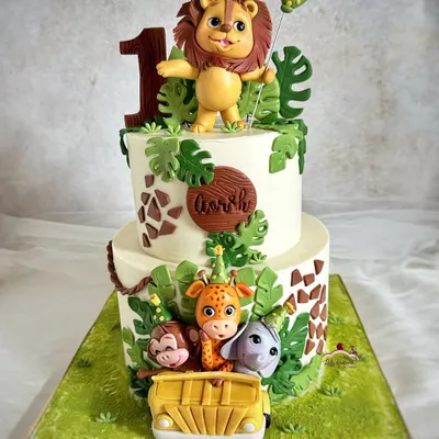 A safari cake for a roaring first birthday celebration! This two-tier design features a hand-sculpted lion topper and a jeep full of his adorable animal friends.