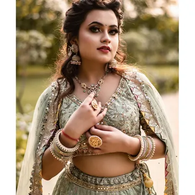 This portrait captures the regal elegance of a beautifully detailed lehenga. Shot outdoors, the soft natural light complements the pastel green fabric and intricate gold jewelry, creating a look of timeless grace.