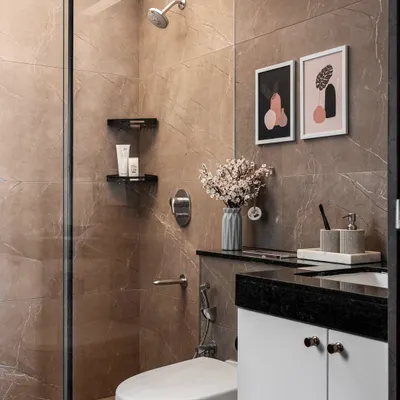 A modern and minimalist bathroom with neutral-toned marble-look tiles. The space includes a glass-partitioned shower and a compact vanity with simple, elegant decor.