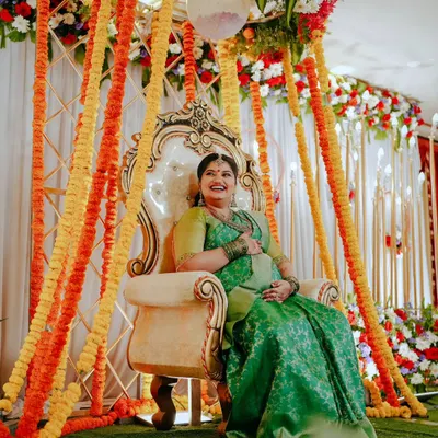 The mother-to-be looking radiant on an ornate throne during her Sreemantham ceremony. The vibrant floral decor with marigolds and roses creates a festive and traditional atmosphere.